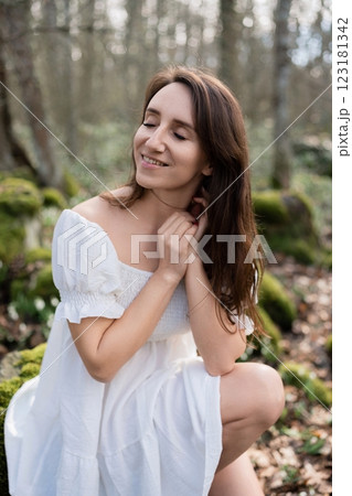 Portrait of a woman in the forest. She is sitting in a white dress on a meadow with snowdrops in a spring forest 123181342
