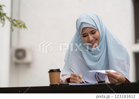 Muslim businesswoman reviewing documents and taking notes with coffee cup. Muslim businesswoman reviewing documents and taking notes with coffee cup. 123181612