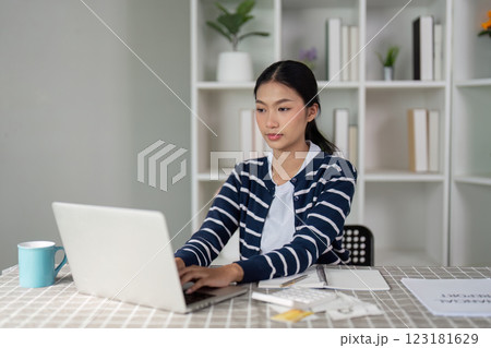 Young woman focused on financial planning and bills while typing on laptop at home. 123181629