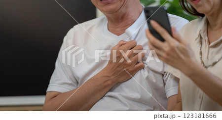 Elderly man smiling while holding his chest, woman on phone in supportive role. Elderly man smiling while holding his chest, woman on phone in supportive role. 123181666