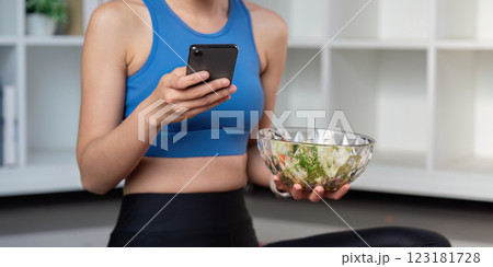 Health conscious woman enjoying a salad while using her smartphone, promoting healthy eating habits. 123181728