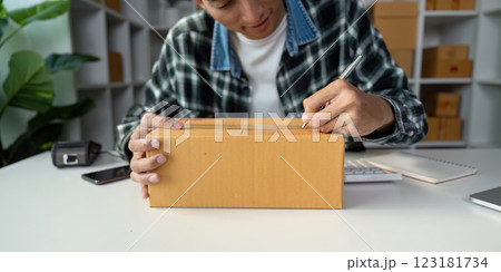 Person carefully labeling cardboard box for online order shipment, showcasing attention to detail. Person carefully labeling cardboard box for online order shipment, showcasing attention to detail. 123181734
