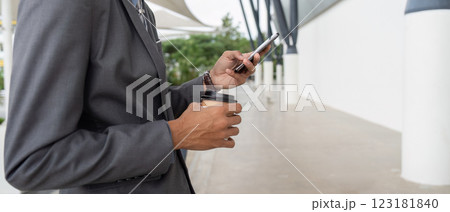 Businessman holding coffee cup and smartphone while standing outdoors. Businessman holding coffee cup and smartphone while standing outdoors. 123181840
