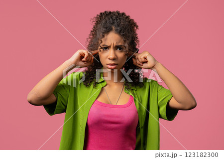 Irritated young african woman covering ears ignoring on pink. Noise, shouts 123182300
