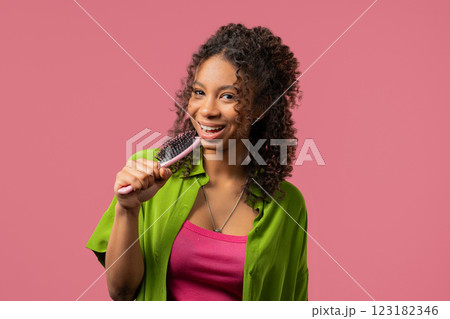 African teenager girl singing, dancing with hairbrush as microphone on pink 123182346