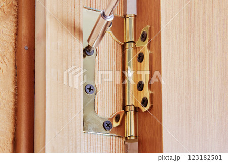 Brass hinges are attached to wooden door frame with metal screws, showing joint mechanism for door movement. Brass hinges are attached to wooden door frame with metal screws, showing joint mechanism for door movement. 123182501