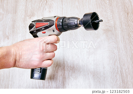 Hand holds cordless drill with hole saw attachment. Hand holds cordless drill with hole saw attachment. 123182503