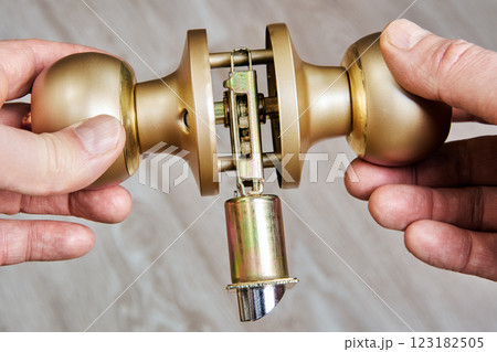 Brass doorknob assembly shown with internal mechanism exposed, hands holding knobs for installation or repair on wooden surface. 123182505