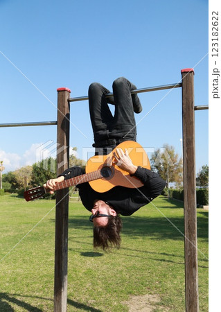 Young Man Plays Guitar Music Hanging Upside Down In An Outdoor Park 123182622