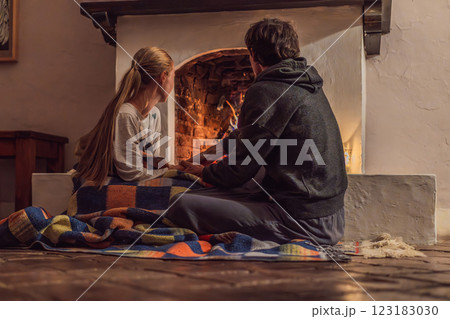 Family bonding by the fireplace during cozy winter evening. Warm and peaceful family moment indoors. Togetherness, love, and relaxation concept. A warm and inviting scene featuring a lit fireplace 123183030