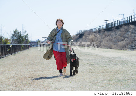 青空の河川敷で散歩を楽しむ女性とカメラ目線の犬　全身　2人で笑顔 123185660