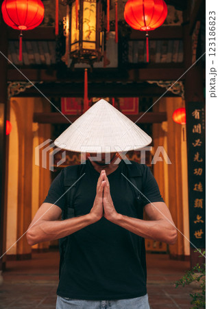 male tourist traveler in a Vietnamese hat prays at temple on a Buddhist pagoda in Hoi An in Vietnam in Asia 123186823