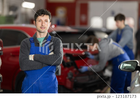 Auto mechanic in uniform standing by automobile in car workshop 123187173