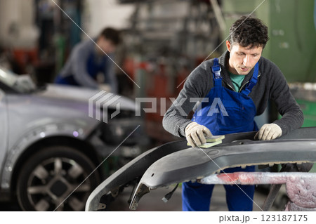 Car bumper repair in car service - professional car painter polishes and prepares bumper before painting 123187175