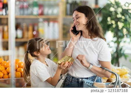 While choosing products, woman talks on phone and does not pay attention to her daughter. While choosing products, woman talks on phone and does not pay attention to her daughter. 123187188