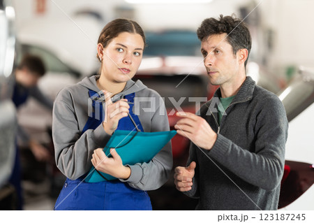 Girl employee asks clarifying questions and writes down male clients wishes regarding car repairs Girl employee asks clarifying questions and writes down male clients wishes regarding car repairs 123187245