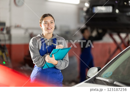 Female car service worker keeps records of work performed by auto mechanics in car service station - makes notes on paper 123187256