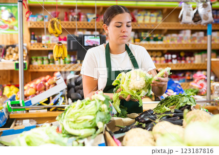 Hardworking young saleswoman puts cabbage on the counter Hardworking young saleswoman puts cabbage on the counter 123187816