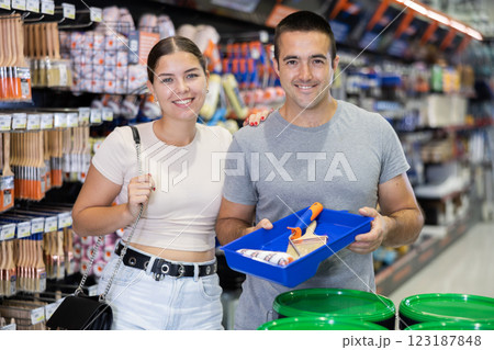 Cheerful couple standing in construction hypermarket with painting tools 123187848
