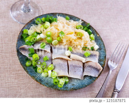 On table is plate with pieces of salted herring fillet and stewed cabbage and green onion 123187871