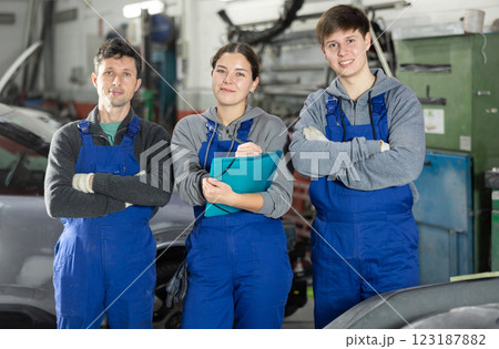 Team of auto mechanics, two men and one woman, wearing blue overalls and posing, ready to provide professional vehicle service 123187882