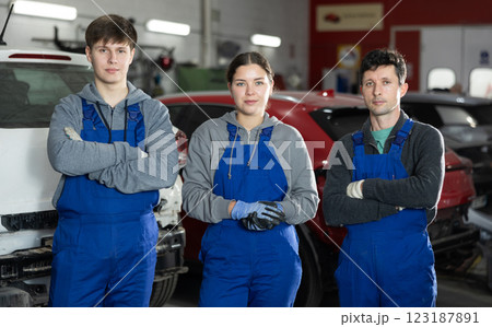 Team of auto mechanics, two men and one woman, wearing blue overalls and posing, ready to provide professional vehicle service 123187891