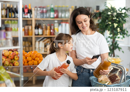 Mother and daughter choose bottles of juice and scan QR code with smartphone in supermarket 123187911
