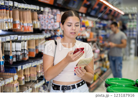 Female shopper scans QR code with her phone to check product information. Buying paint brushes at hardware store 123187916
