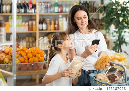 Mother and daughter checks expiration date of cornflakes and oat flakes - scans QR code on label 123187928