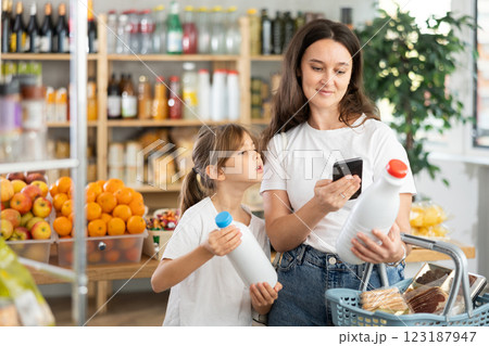 Girl with mother customers at shop scans QR code on milk package using phone camera Girl with mother customers at shop scans QR code on milk package using phone camera 123187947