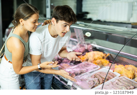 Spouse near butcher shop window inspects goods and choose sausages for grill Spouse near butcher shop window inspects goods and choose sausages for grill 123187949