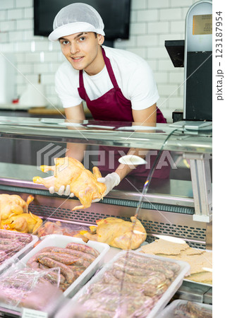 Positive young salesman demonstrating chicken in butcher shop Positive young salesman demonstrating chicken in butcher shop 123187954