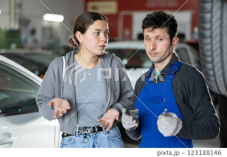 Man car mechanic talks with girl client in workshop and takes order. 123188146