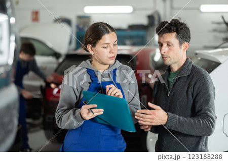 Girl employee asks clarifying questions and writes down male clients wishes regarding car repairs 123188288