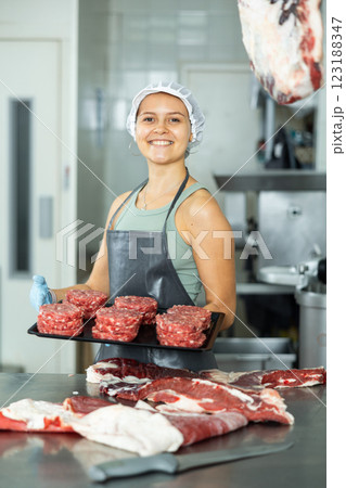 Saleswoman of butcher shop stands with tray and round blanks of ground beef, raw minced calf patties Saleswoman of butcher shop stands with tray and round blanks of ground beef, raw minced calf patties 123188347