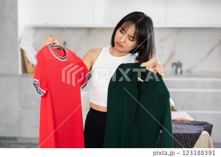 Sad young Asian girl trying to choose a dress in the kitchen 123188391