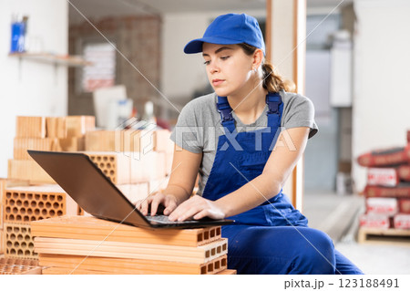 Young woman builder sitting on bricks and using laptop 123188491