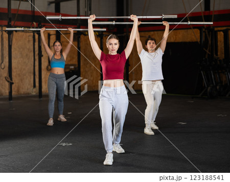 Slender girl trains muscles of arms and back using barbell and differentiated weighting in gym 123188541