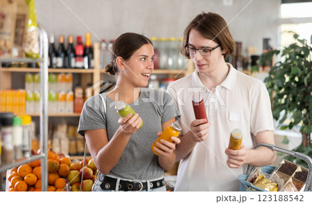 Youth girl and guy friends hold packages bottles and choose consider smoothie in store Youth girl and guy friends hold packages bottles and choose consider smoothie in store 123188542