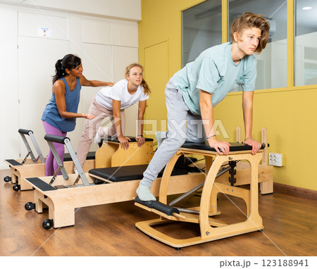 Teen boy and girl in sportswear keeps the balance, pilates training on exercise machine in gym. Fitness workuot in sport gym Teen boy and girl in sportswear keeps the balance, pilates training on exercise machine in gym. Fitness workuot in sport gym 123188941
