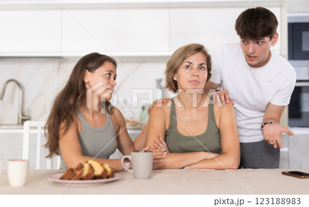 Sad mom sits silently in kitchen, adult children, guy and girl sympathize and comfort woman Sad mom sits silently in kitchen, adult children, guy and girl sympathize and comfort woman 123188983