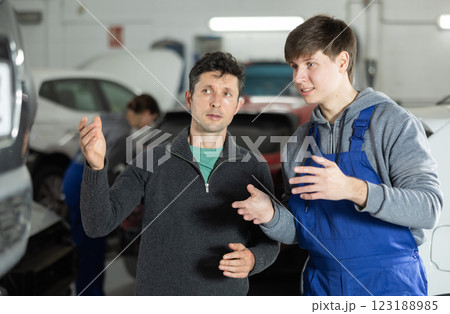 Adult car owner discusses with a young auto mechanic the cost and time of car repairs at car service center 123188985