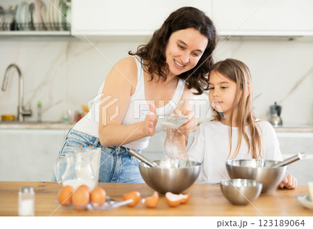 Happy mother and her daughter adding flour in metal bowl and whisking ingredients in the kitchen Happy mother and her daughter adding flour in metal bowl and whisking ingredients in the kitchen 123189064