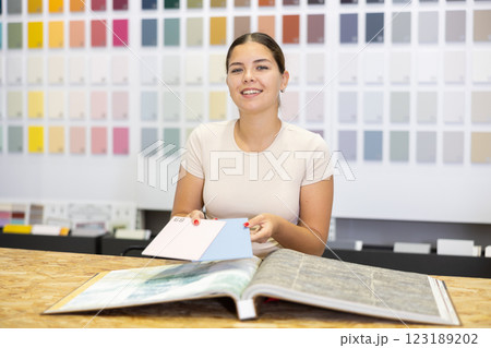 Friendly female seller in a hardware store offers to choose the color of ceramic tiles from catalog 123189202