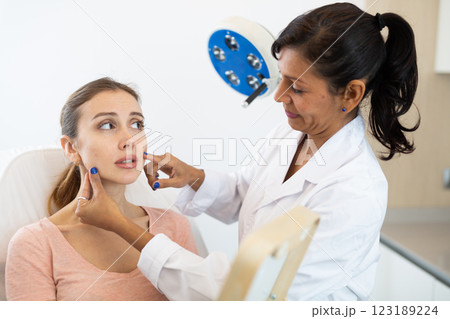 Cosmetologist examining face of young woman Cosmetologist examining face of young woman 123189224