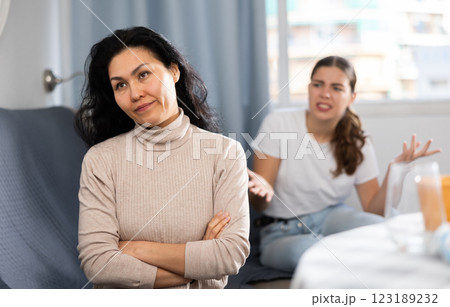 Upset woman sitting at home table with disgruntled woman behind Upset woman sitting at home table with disgruntled woman behind 123189232