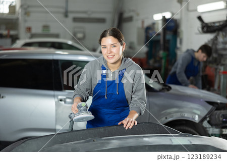 Young woman auto mechanic polishes body parts by car buffer polisher machine tool 123189234