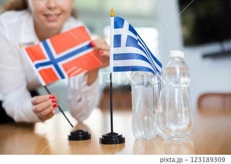 Unrecognizable girl sets midget flags of Greece and Norway before international negotiations 123189309