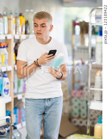 Positive young man buyer in shop holding and choosing shampoo or shower gel, scan QR code on label 123189422
