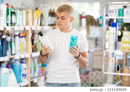 Young man looking shampoo or shower gel, standing near shelves in beauty store 123189694